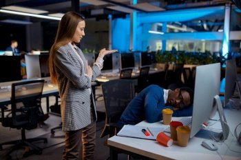 Woman looks on sleeping manager, night office lifestyle. Tired male persons at laptop, dark interior on background, modern workplace. Woman looks on sleeping manager, night office