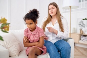 Mother scolds her little daughter on sofa in living room.Mom and sad female child, difficulties of raising children. Mother scolds her little daughter in living room