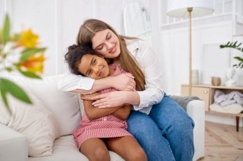 Happy mother hugs her little daughter on sofa in living room.Mom and female child leisures in their house together, good relationship, parental care. Mother hugs her little daughter in living room