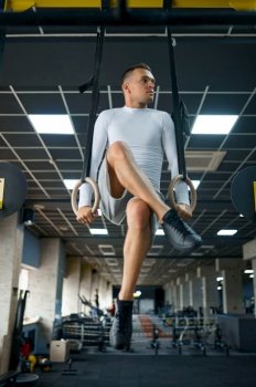 Muscular man doing endurance exercise on the rings, fitness training in gym. Athletic male person on workout, sportsman in sport club, active healthy lifestyle, physical wellness. Muscular man doing endurance exercise on the rings