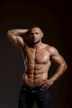 Male athlete with muscular body poses in studio, dark background. One man with athletic build, shirtless sportsman in jeans pants, active healthy lifestyle. Male athlete with muscular body poses in studio