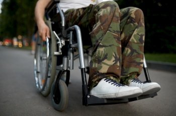 Disabled soldier, view on legs. Paralyzed people and disability, handicap overcoming. Disabled man in the park. Young male person in wheelchair, view on legs