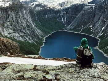 Man sits at the end of Trolltunga before the mountains