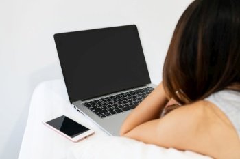 Closeup of young Asian woman using computer on bed in the morning. Technology and lifestyle, work from home concept. Copy space