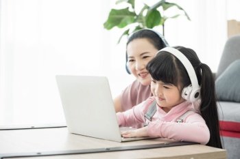 asian girl studying with laptop and headset ,correspondence course with social distancing, mother sit beside and teach together.