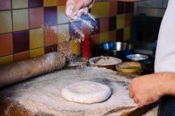 Male hands spread the flour and make dough for pizza. Falling flour.