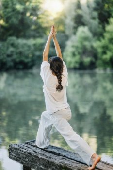 Yoga by the Lake – Young woman practicing Warrior 1 Pose or Virabhadrasana I. Yoga by the Lake – Young woman practicing Warrior 1 Pose