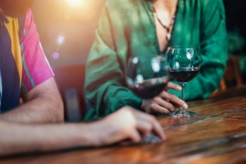 Cropped shot of couple drinking red wine at wooden restaurant table. Wearing colorful outfit. 