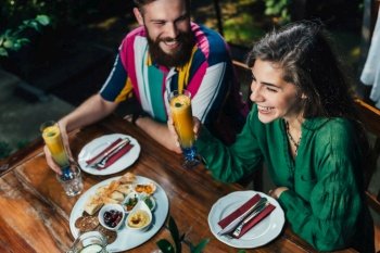 Young smiling couple enjoying romantic vegetarian dinner.  Couple sitting at wooden table, wearing colorful outfit.  