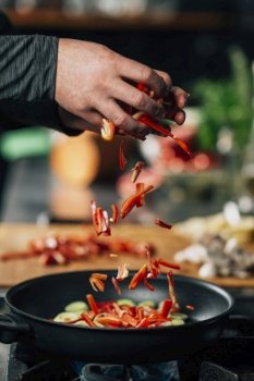 Vegan restaurant cooking. Chef’s hand adding sliced red bell peppers into a frying pan.. Vegan Restaurant Cooking - Adding Sliced Red Bell Pepper into a Frying Pan 