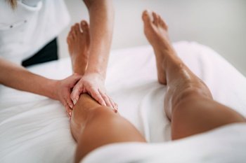 Physiotherapist massaging female patient with injured leg. Sports injury treatment.. Legs Sports Massage Therapy