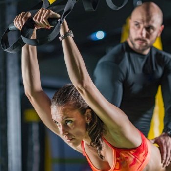  Personal trainer exercising on TRX with woman in the gym