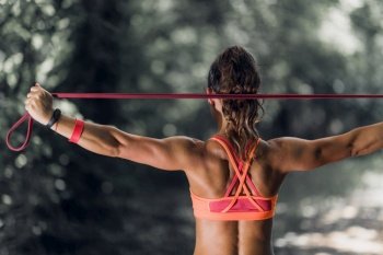Outdoor exercising. Female athlete exercising with elastic band in the park