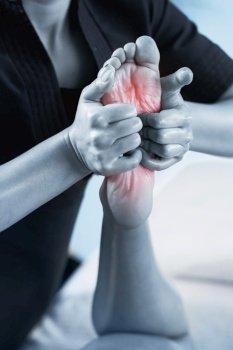 Close up image of physiotherapist massaging female patient with injured foot. Blue colored image. Red accent on the sole foot pain. Sports injury treatment.