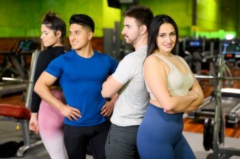 Group of young athletic female and male adults standing together as good friends in gym after workout session. High quality photo. Group of young athletic female and male adults standing together as good friends in gym after workout session