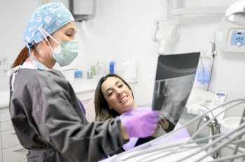 Female dentist pointing at patient’s X-ray image in dental office. High quality photo. Female dentist pointing at patient’s X-ray image in dental office.