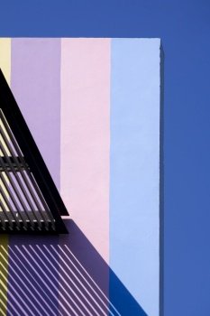 Sunlight and shadow of awning on surface of colorful building wall against blue sky in vertical frame, Abstract architecture background and building exterior concept
