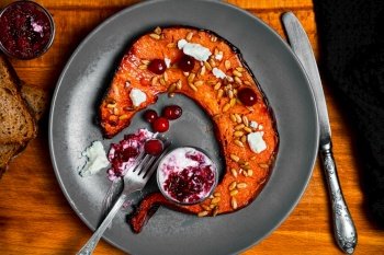 Slice of oven-baked pumpkin with feta cheese, cranberries and sunflower seeds on a plate with cranberry and cream sauce. Traditional Northern European cuisine. Top view