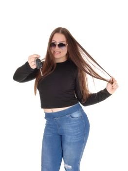 A young teenage girl got the keys for her new car holding them up, standing in jeans and black swather, isolated for white background