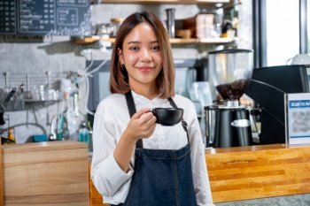 Portrait of barista woman or coffee maker hold a cup and stand in front of counter in coffee shop with looking at camera and smile.