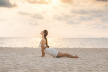Asian young woman practice Cobra Pose on the sand and beach with sunset beautiful sea in Tropical island,Feeling comfortable and relax in holiday,Vacations Yoga Concept