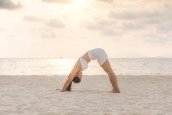 Vacation of Attractive Asian woman relaxing in yoga Downward Facing dog or Adho Mukha Svanasana pose on sand and beach with sunset sea in Thailand Tropical island,Feel comfortable and relax in holiday
