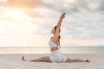 Asian young woman practice Yoga Monkey God Pose or Yoga Hanumanasana pose on the sand and beach with sunset beautiful sea in Tropical island,Feel comfortable and relax in holiday,Vacation Yoga Concept