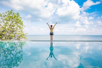 Portrait of Asian young woman standing on the pool above the beach feeling so happiness and cheerful,Travel in tropical beach in Thailand,vacations and relaxation Concept