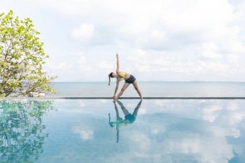 woman practice yoga Triangle pose to meditation summer vacation on the pool above the beach,Travel in tropical beach Thailand,vacations and relaxation Concept