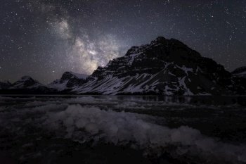 Icy blocks along the shore of Bow Lake with the Milky Way shining behind the Canadian Rockies along the Icefields Parkway in Banff National Park.