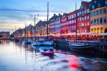 Evening scene with boats moored by illuminated Nyhavn harbor embankment, Copenhagen, Denmark