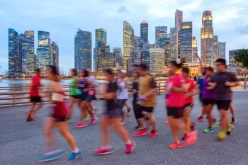 Joggers running on illuminated promenade, Singapore downtown core on background