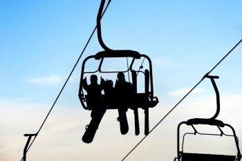 Silhouettes of people with skis and snowboards on chairlift against sky, Bukovel, Ukraine 