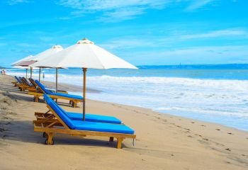 Deck chairs under parasols on sandy beach of tropical resort, Bali island, Indonesia