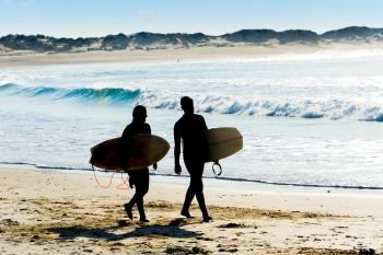 Couple of surfers walking by the ocean beach. Portugal