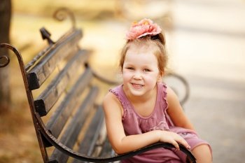 Portrait of a smiling pretty little girl sitting on a park bench