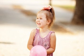 Portrait of laughing and playing a little girl holding a pink balloon. Positive emotions. Happy child.
