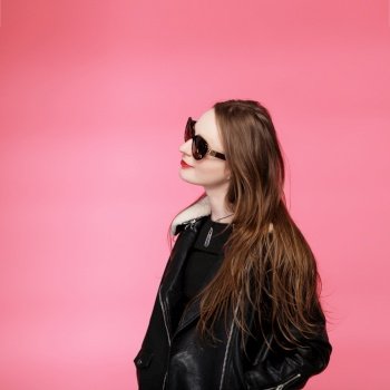fashion model wearing black in sunglasses, beautiful young woman. leather jacket, studio shot, pink background