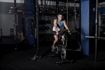 Adult confident sportsman riding stationary bicycle in modern dark gym. Sportsman riding stationary bicycle in gym