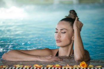 Pretty female with closed eyes touching wet hair while enjoying spa procedure in swimming pool. Sensual woman touching wet hair in pool 