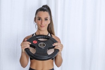 Positive young sporty female demonstrating heavy weight disk during functional workout at home. Fit woman with weight plate