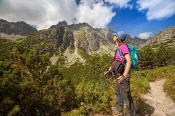 Happy woman with backpack standing and looking on high rocky peaks near Zelene Pleso in Tatra Mountains, Slovakia, Europe. Hiking woman admiring the beauty of rocky mountains