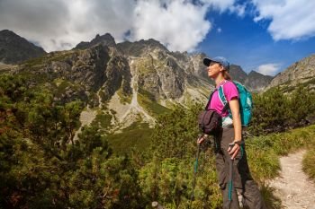 Happy woman with backpack standing and looking on high rocky peaks near Zelene Pleso in Tatra Mountains, Slovakia, Europe. Hiking woman admiring the beauty of rocky mountains