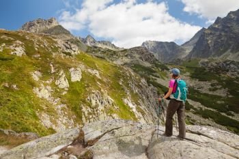Happy woman with backpack standing and looking on high rocky peaks in Tatra Mountains, Slovakia, Europe. Hiking woman admiring the beauty of rocky Tatra mountains