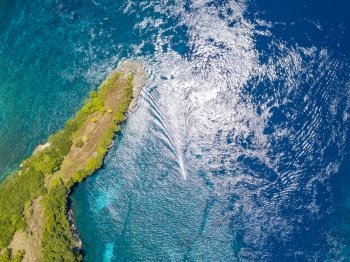 Indonesia. Emerald surface of the ocean. A small boat trimaran near a tropical island, overgrown with jungle. Aerial view vertically down. Island in the Ocean and a Boat Trimaran. Aerial View