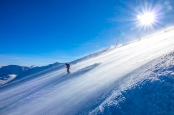 Steep ski slope and bright sun. Snowstorm on the surface. Skier rides down. Skier on a Sunny Slope and Blizzard