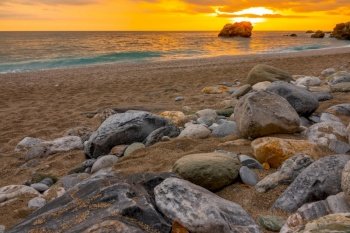 Beach with coarse sand and colorful stones. Golden sunset over the calm sea. Sunset Over the Calm Sea and Colorful Stones on the Sandy Beach