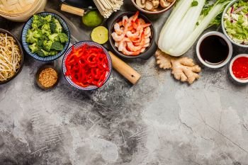 Asian cuisine ingredients on grey stone background, top view. Vegetables, spices, shrimp, noodles, sauces for cooking vietnamese, thai or chinese food. Clean eating food concept