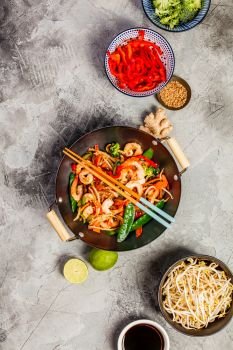 Stir fry with prawns, vegetables, soy sause and sesame in the wok. Traditional asian food. Top view on grey stone background.