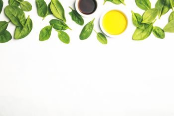 Cooking ingredients on white background: olive oil, vinegar and spinach. Vegan food, vegetarian and healthily cooking concept. Top view